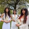 three women in white dresses stand outside holding masks, part of Terpsikores_Work in progress What the Land still Knows